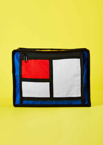crafted from durable cotton canvas and influenced by Piet Mondrian's Colorblock art. The bag showcases a striking composition of intersecting lines and vibrant color blocks, offering a contemporary and eye-catching design